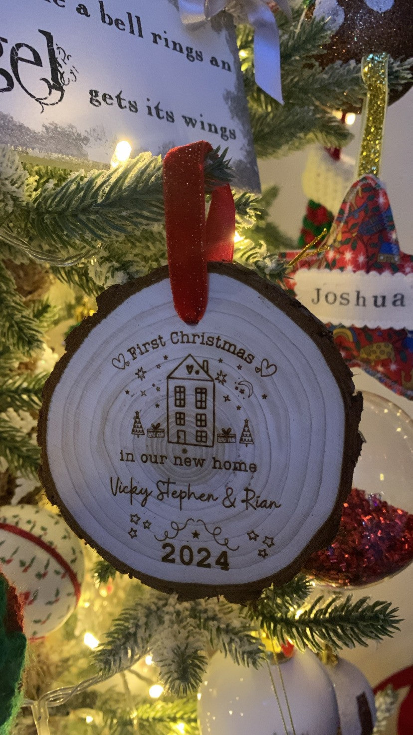 Wooden engraved Christmas ornament on a decorated tree, engraved with “First Christmas in Our New Home.”