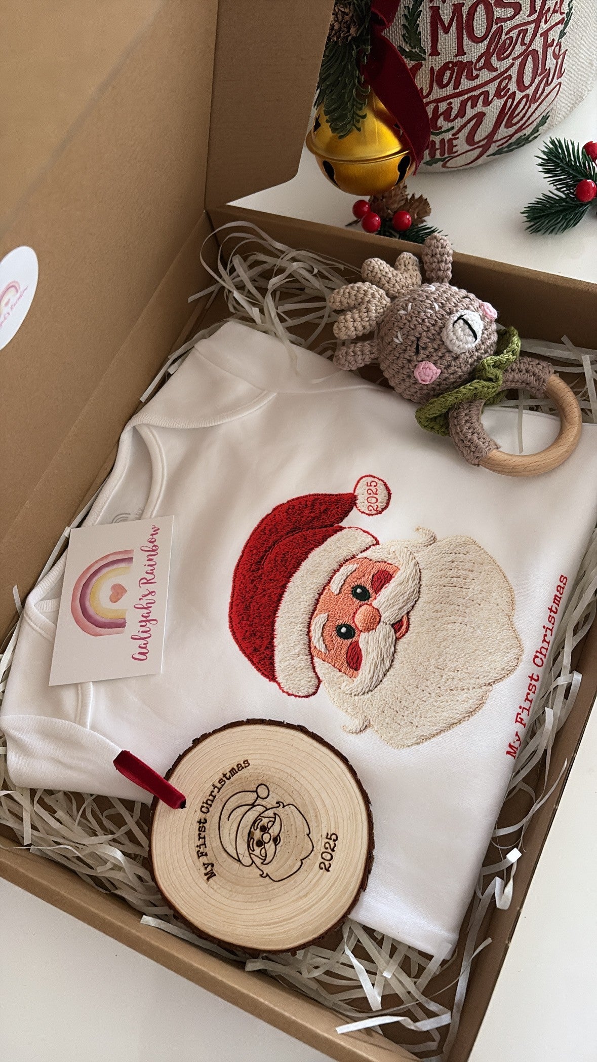 Baby’s First Christmas Gift Set featuring a Santa baby vest, crochet reindeer rattle, and personalised wooden engraved disc in festive packaging.