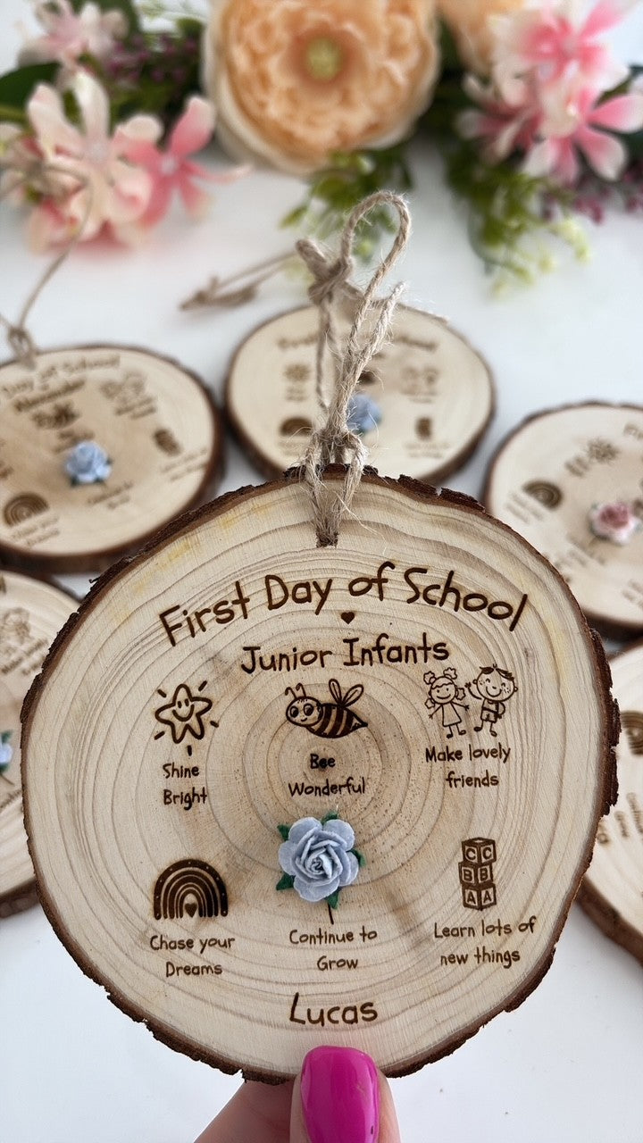 Personalised First Day of School Wooden Disc engraved with a child's name and class, featuring exclusive Aaliyah's Rainbow illustrations and a blue flower, handcrafted on a natural wood slice with twine for hanging. Perfect for back-to-school photos and keepsake memories.