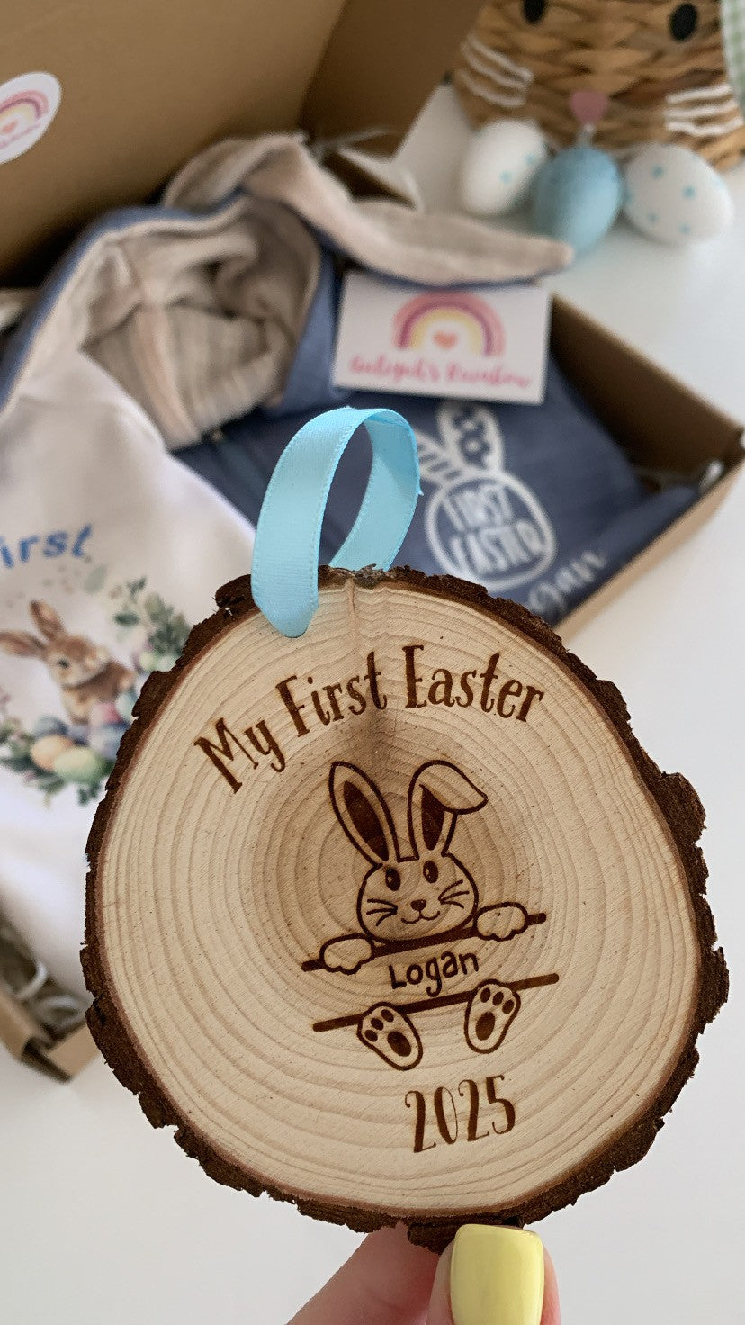 Wooden ornament with engraved text and a rabbit design, held in front of a box with baby items.