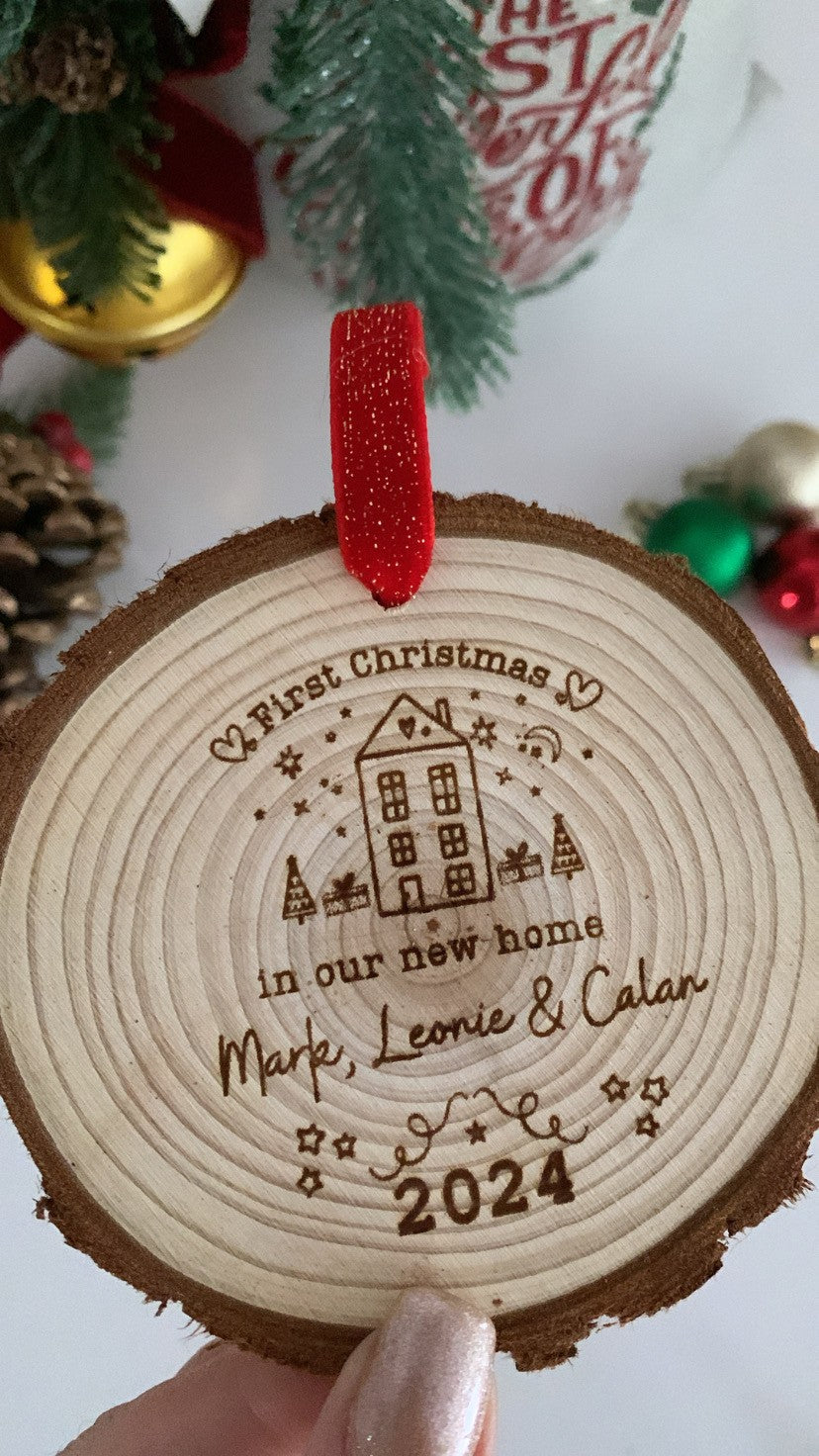 Wooden engraved Christmas ornament on a decorated tree, engraved with “First Christmas in Our New Home.”