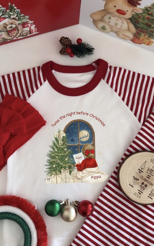 Personalised kids Christmas pyjamas with red and white striped sleeves and illustration of a girl by the tree reading “’Twas the Night Before Christmas.