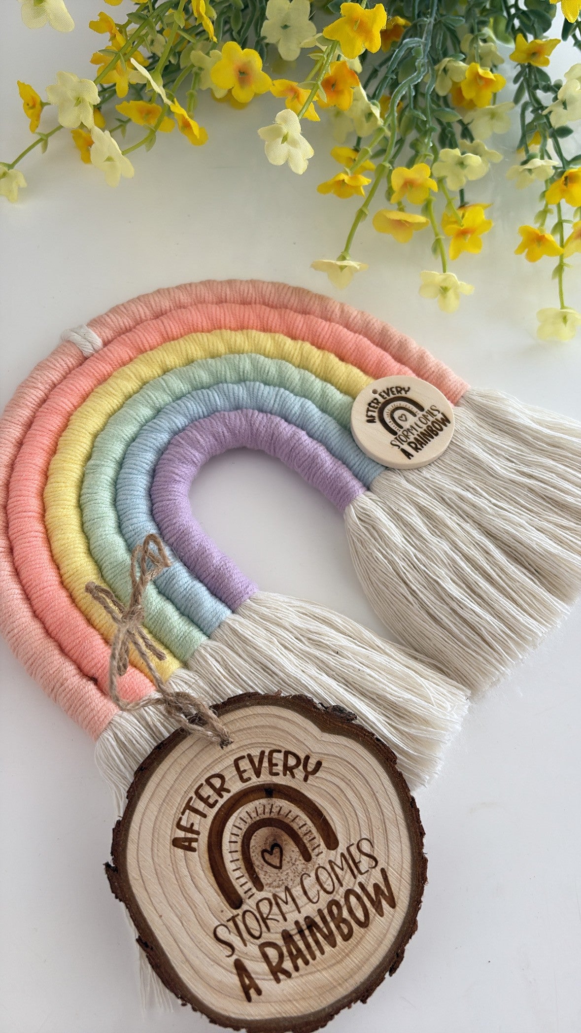 Handmade pastel macrame rainbow wall hanging with engraved wooden tag that reads ‘After every storm comes a rainbow