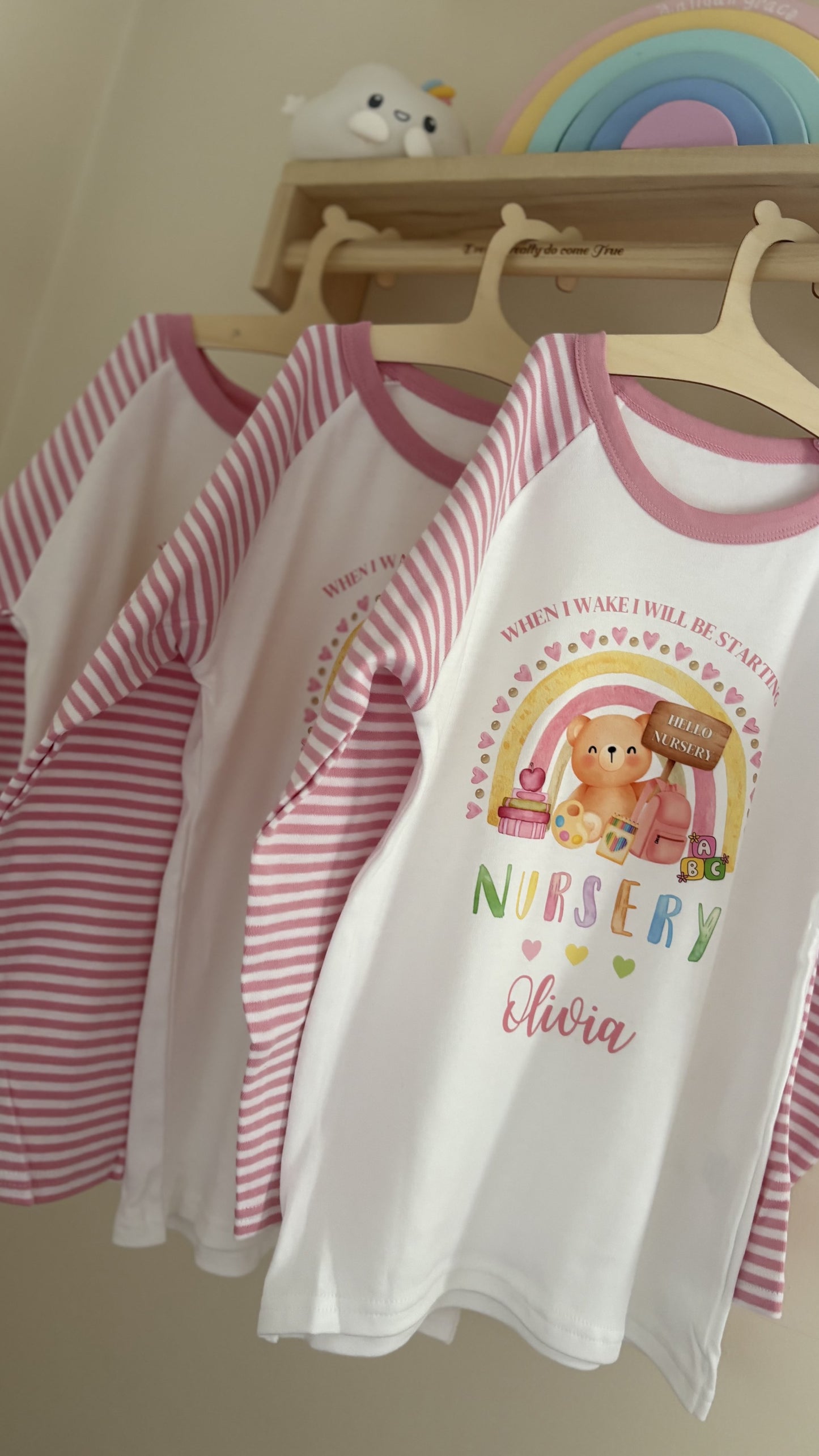 Personalised pink and white striped children's back to school pyjamas featuring a cute teddy bear, rainbow, school backpack and "When I Wake I Will Be Starting Primary 1" design with a custom name, perfect for boys and girls starting school.