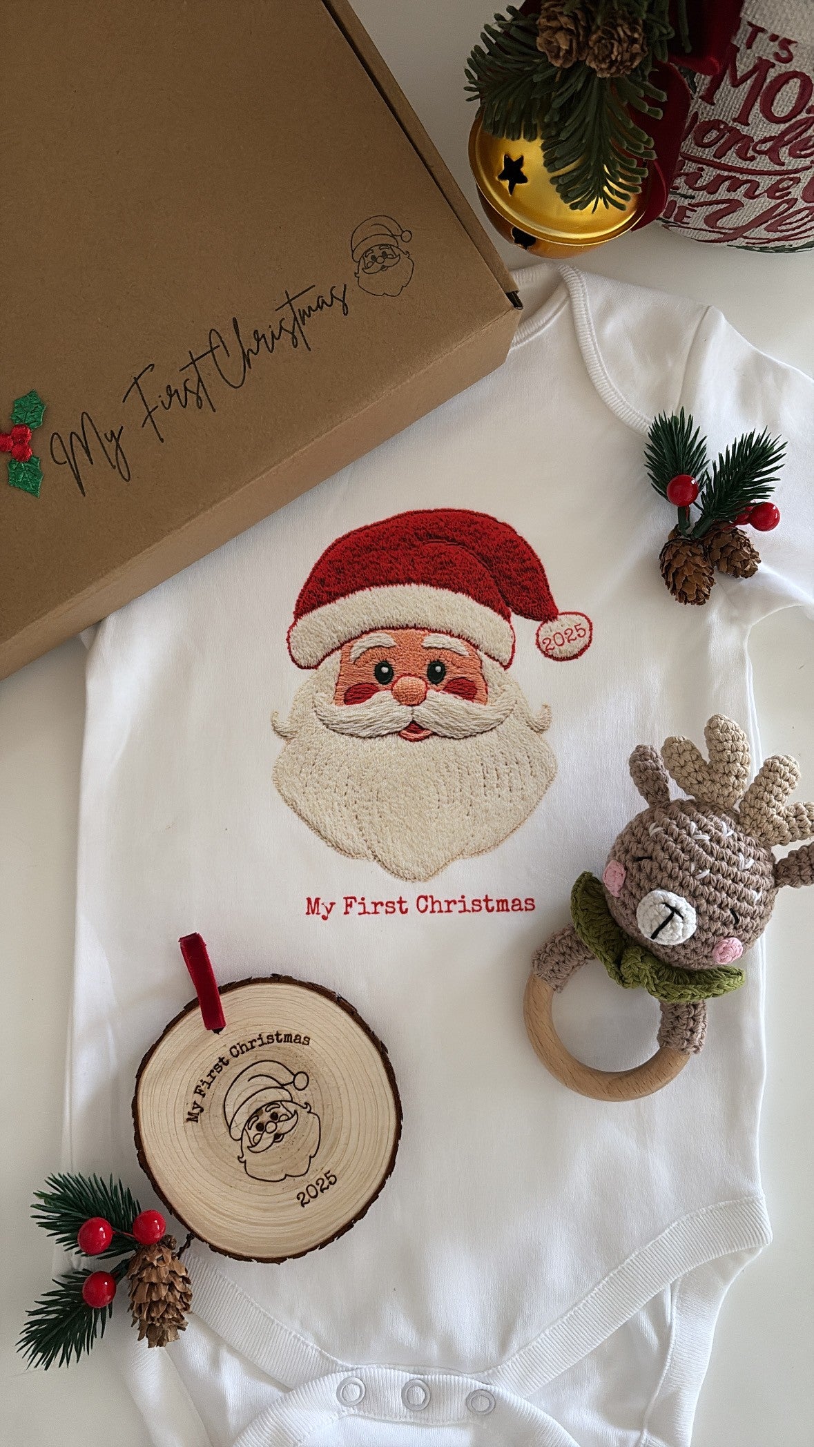 Baby’s First Christmas Gift Set featuring a Santa baby vest, crochet reindeer rattle, and personalised wooden engraved disc in festive packaging.