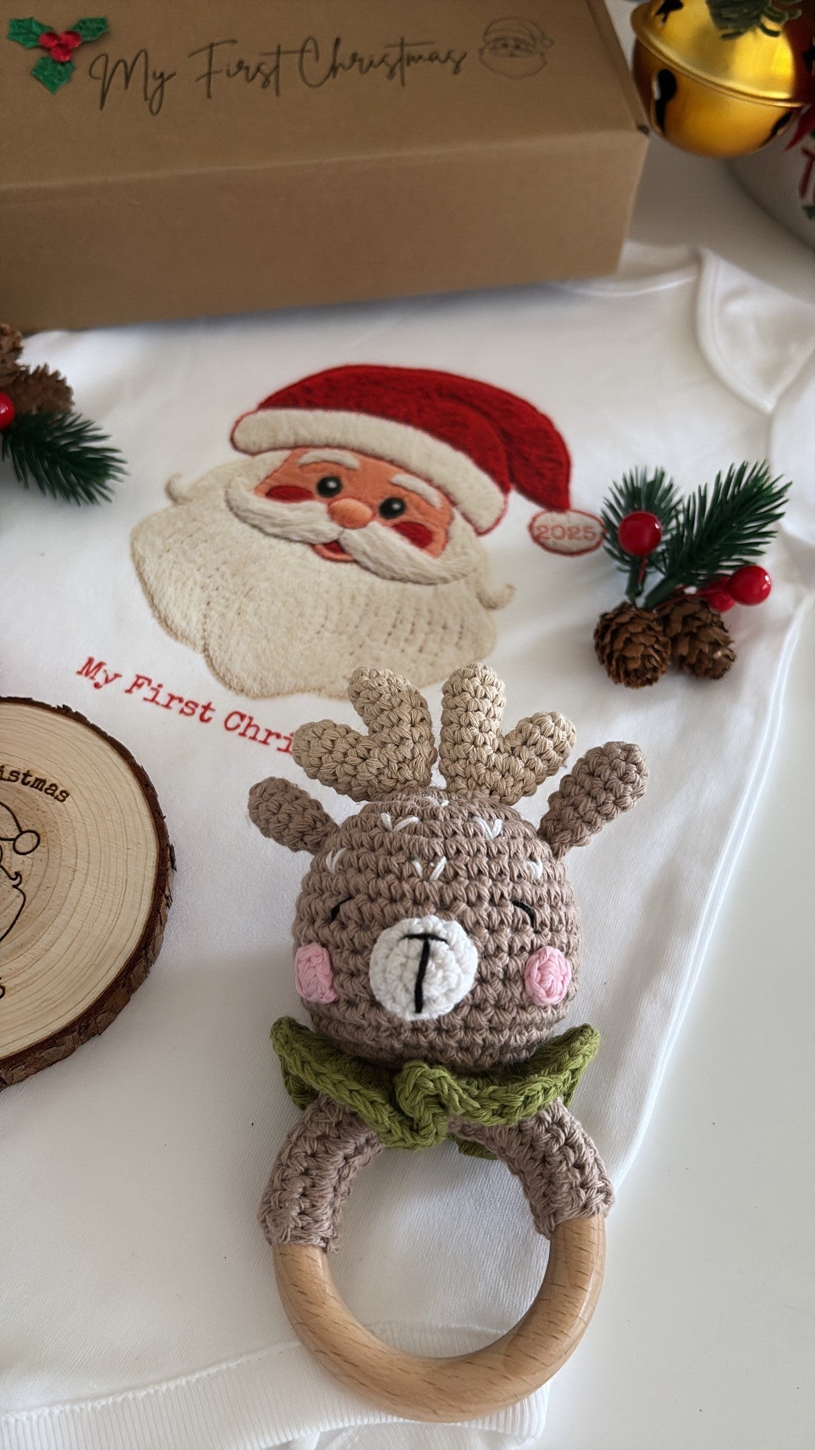Baby’s First Christmas Gift Set featuring a Santa baby vest, crochet reindeer rattle, and personalised wooden engraved disc in festive packaging.
