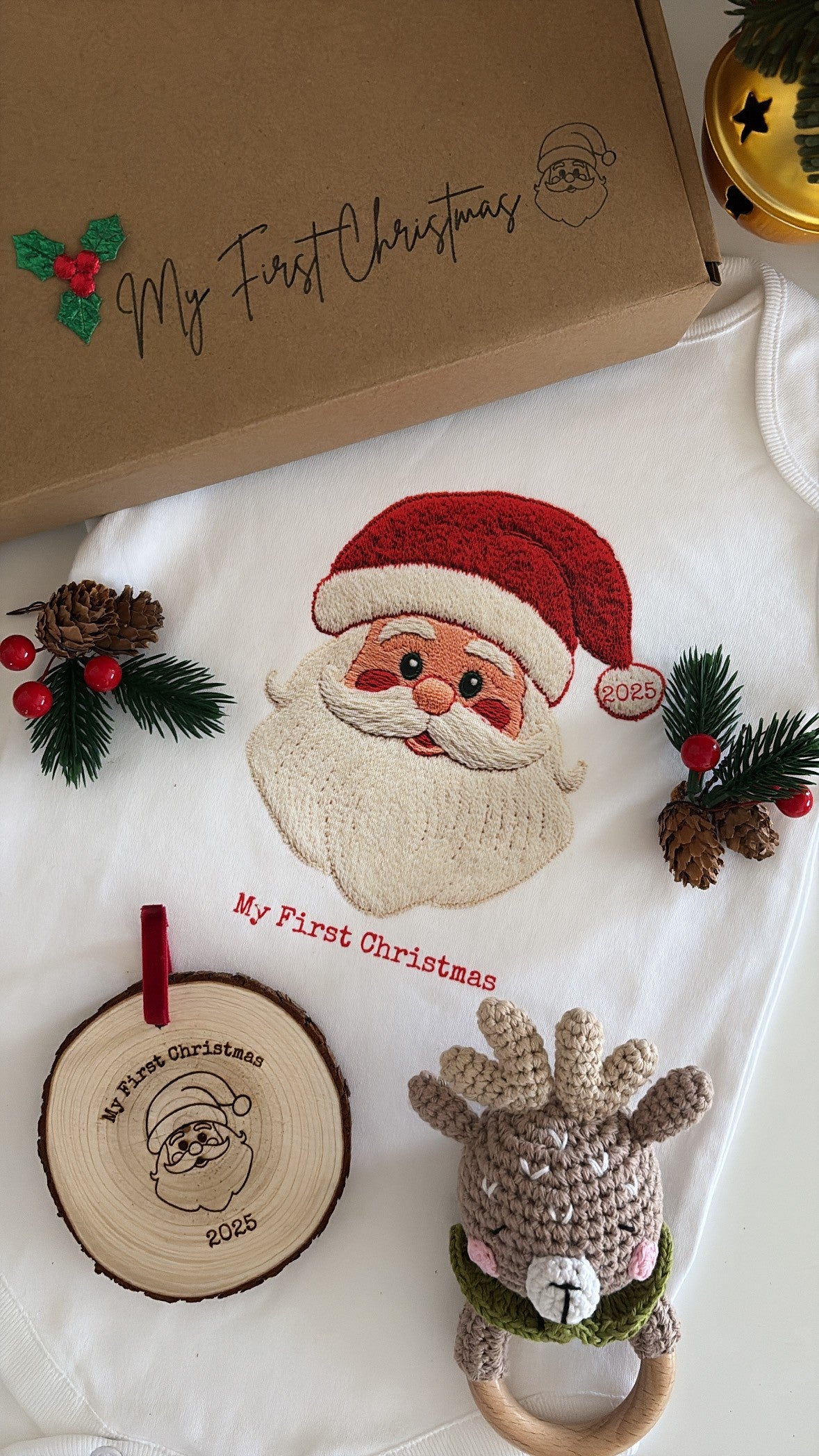 Baby’s First Christmas Gift Set featuring a Santa baby vest, crochet reindeer rattle, and personalised wooden engraved disc in festive packaging.