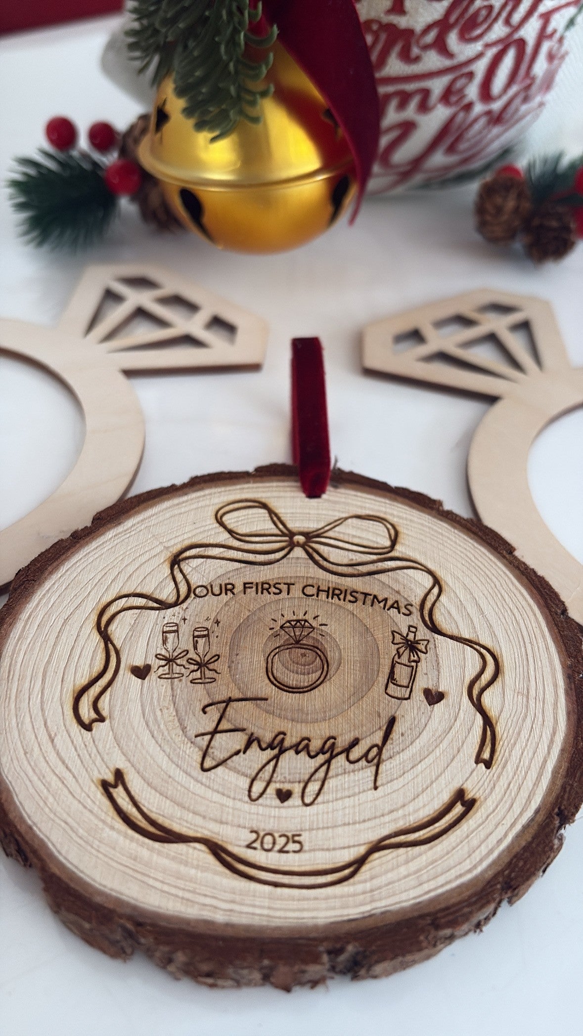 Wooden ornament with 'Our First Christmas Engaged' engraving on a white surface with festive decorations.