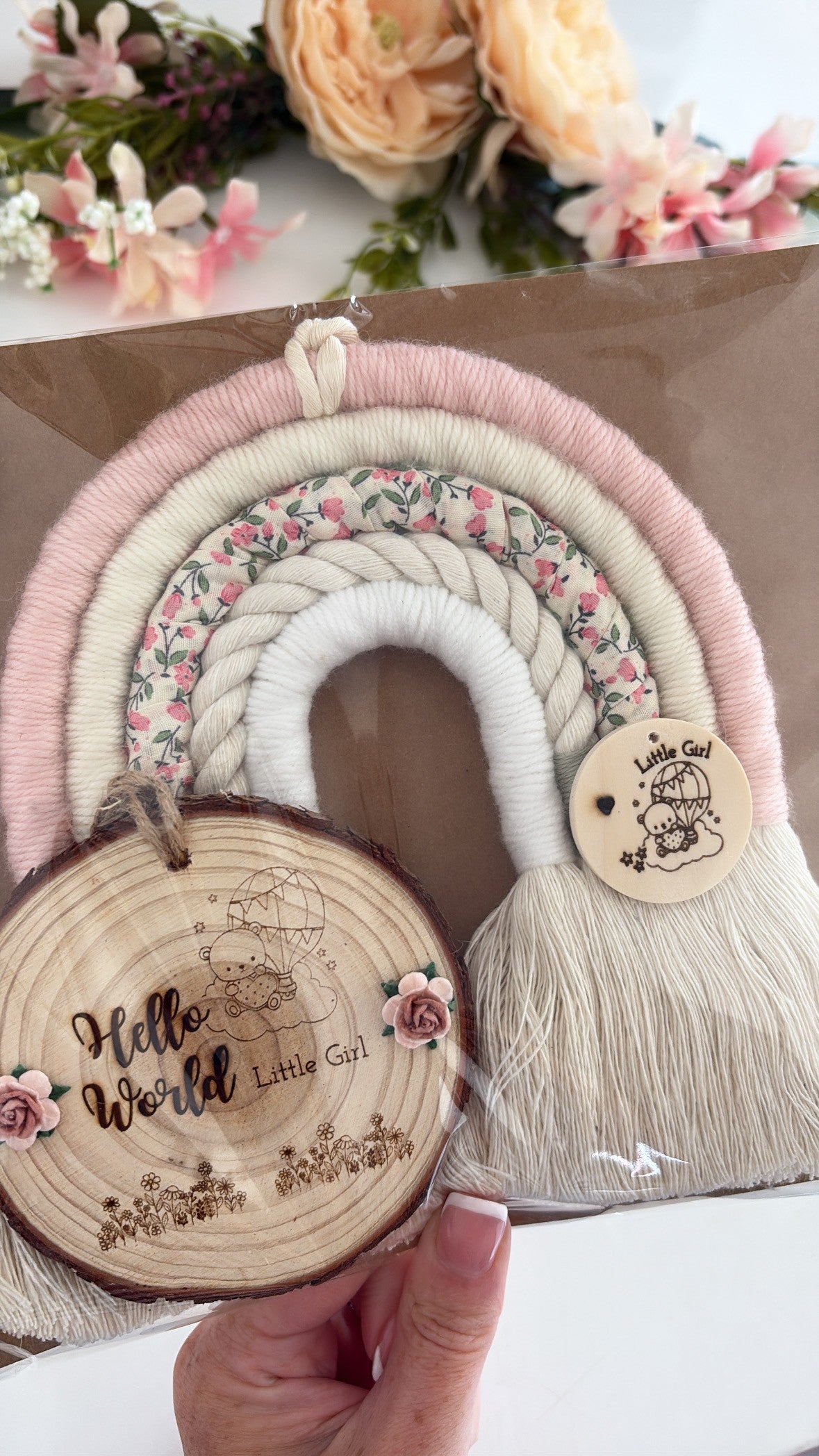 Handmade pink and floral macrame rainbow wall hanging with wooden tag engraved ‘Hello World, Little Girl,’ beautifully wrapped and ready for gifting
