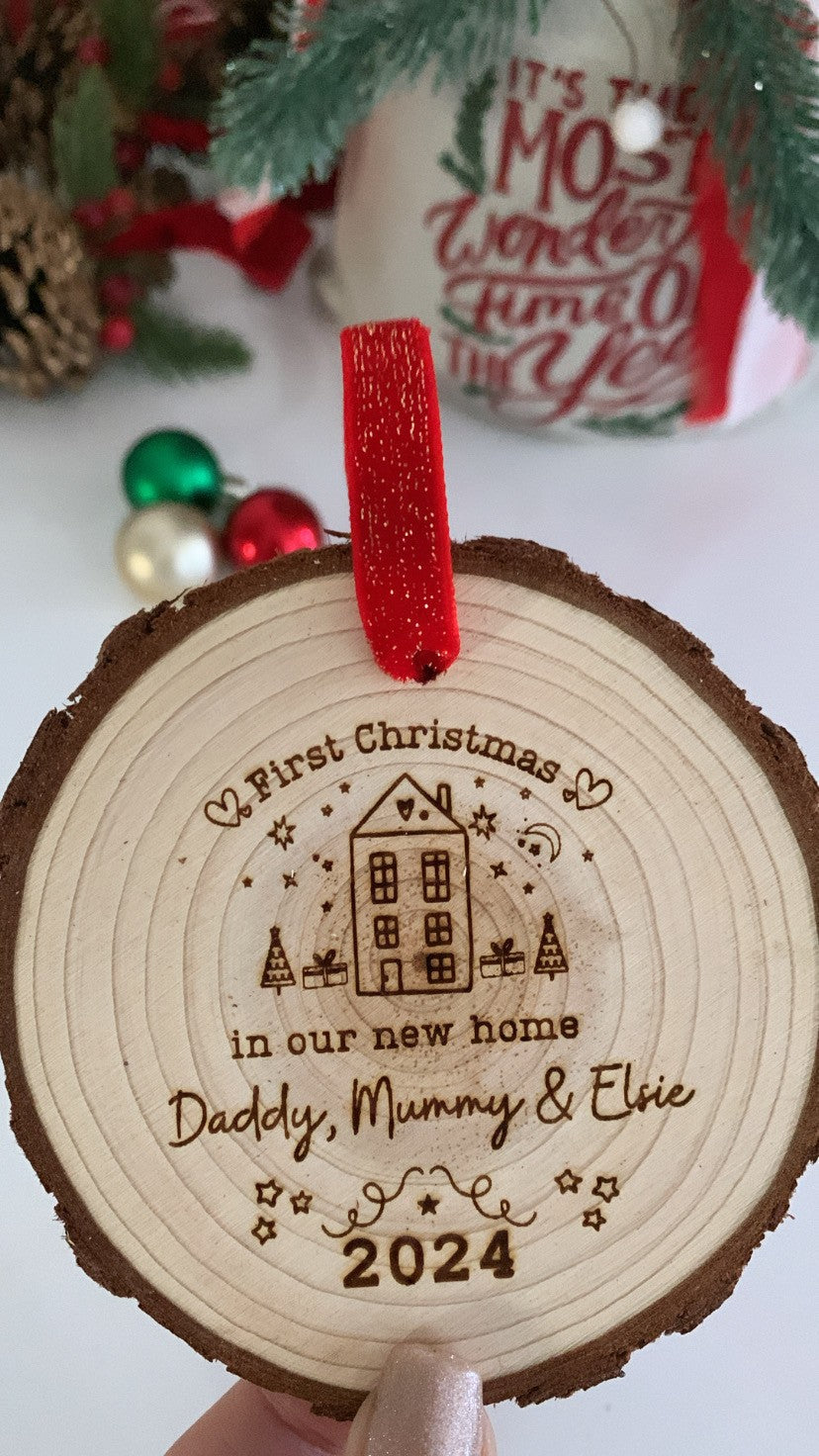 Wooden engraved Christmas ornament on a decorated tree, engraved with “First Christmas in Our New Home.”