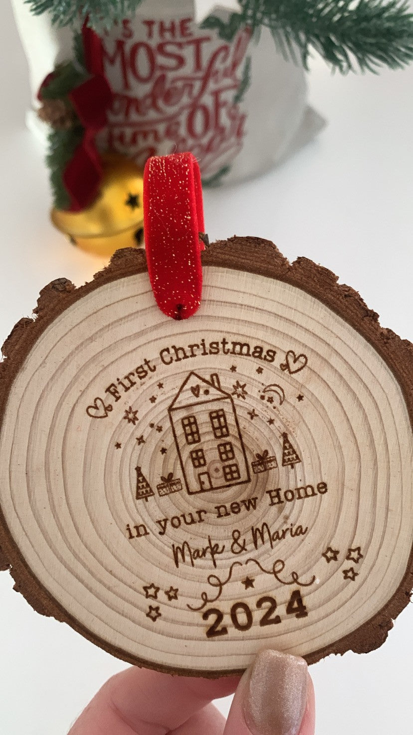 Wooden engraved Christmas ornament on a decorated tree, engraved with “First Christmas in Our New Home.”