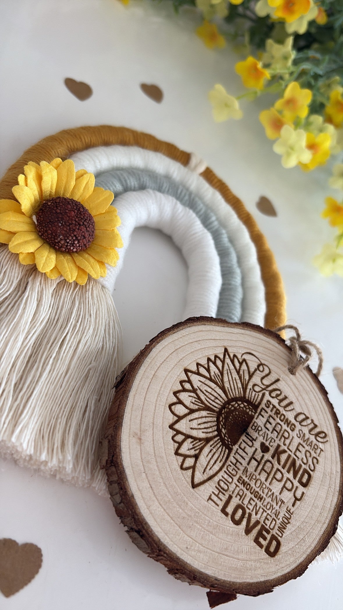 Wooden ornament with sunflower design and engraved text, placed on a white surface with yellow flowers in the background.